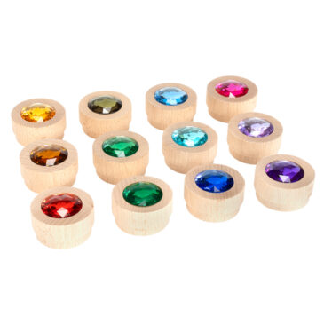 Holz-Funkelsteine Regenbogen 12er Set Die runden in Holz gefassten Funkelsteine ... begeistern die Kinder, denn es sind richtige Schatzsteine. Die Schmucksteine sind stapelbar und eignen sich perfekt für Legespiele, zum Bauen und Spielen, für Weihnachtsdeko, den Einsatz im Jahreszeitenkreis uvm. Ähnlich wie Muggelsteine oder Glasnuggets können mit den 12 farbenfrohen Steinen tolle Muster, und Wege gelegt werden. Außerdem werden sie zum Zählen und Sortieren verwendet. Die Holz-Funkelsteine haben Teelicht-Größe und passen daher wunderbar in Teelichthalter. So bringen die Holz-Funkelsteine nach der Kerzenzeit neuen Glanz auf den Tisch und schmücken Blumen-, Stern- oder Herz-Teelichthalter. Die Kombination mit Bauklötzen und Regenbogen-Material ist eine beliebte Anwendung in der Bauecke. Auf Filzteppichen kommen die Schatzsteine besonders gut zur Geltung. Inhalt: 12 runde stapelbare Holzsteine in 12 Farben.